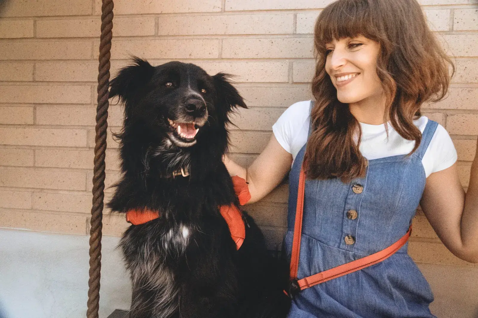 Woman laughing with a black dog in a Canyon harness, wearing a Canyon leash across her body