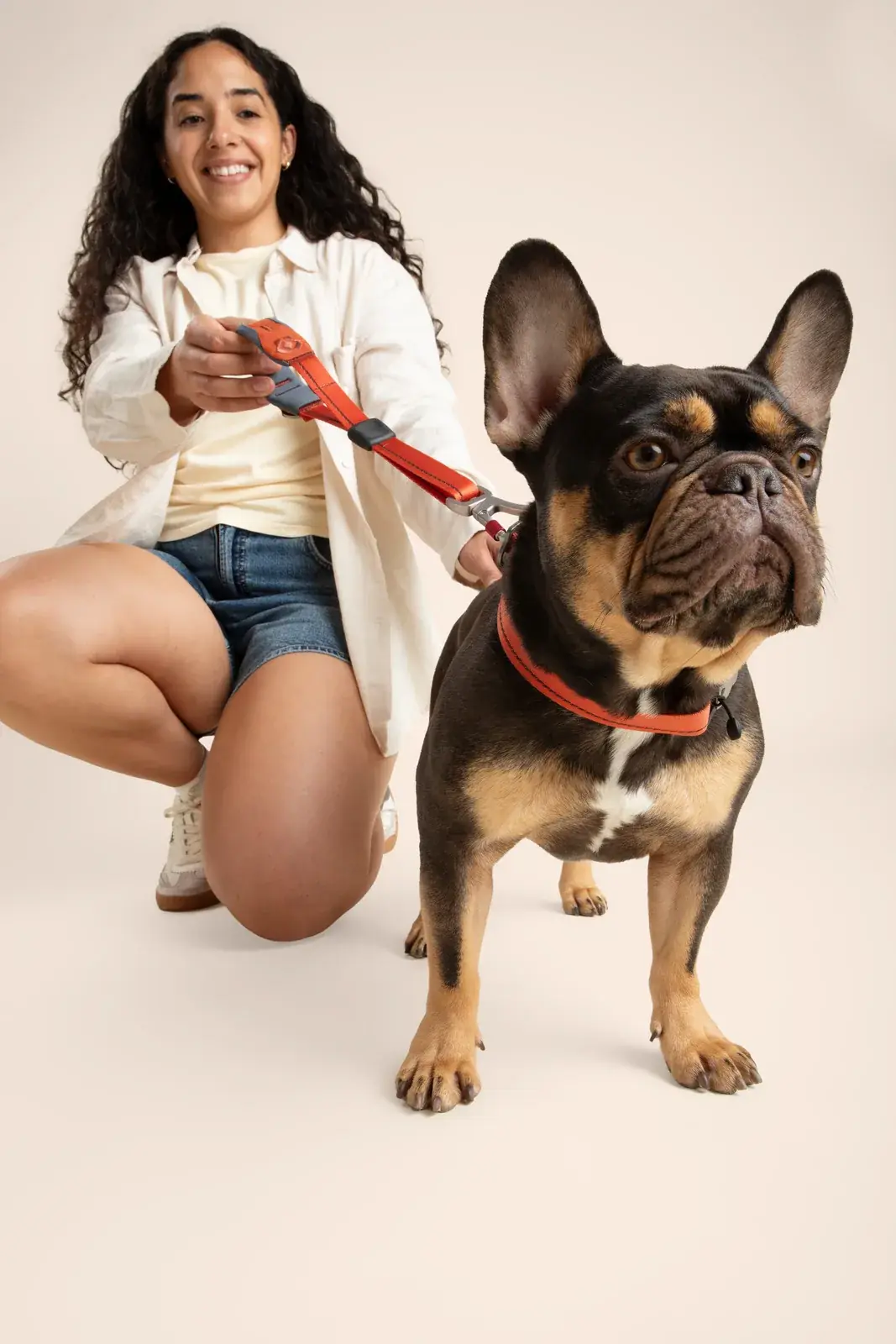 Person kneeling beside a brown french bulldog wearing a Canyon collar with a Canyon quick-grip leash