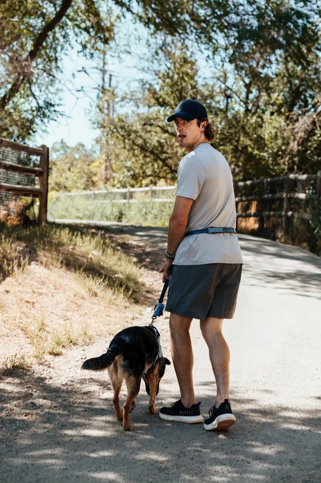 Man walking a black dog in a Coast harness on a Coast leash down a trail