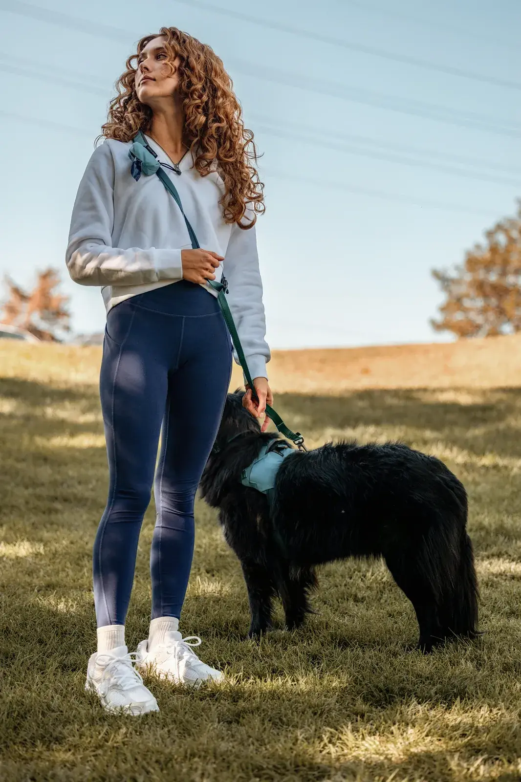 Woman walking a black dog in a Coast harness on a Coast leash across a grassy field